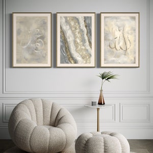 Pu&ograve; includere: Tre stampe d'arte incorniciate con uno sfondo grigio chiaro e calligrafia dorata. Le stampe sono appese a una parete bianca sopra una poltrona e un pouf morbidi bianchi.