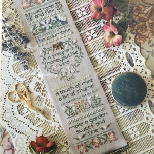 May include: A beige cross-stitch sampler with a floral design and the text "wild rose and flax, the columbine, a fragrant honeysuckle vine, a touch of mint, a bit of thyme, make a garden sweet and fine".