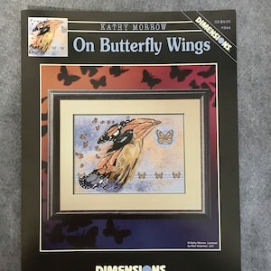 May include: Cross stitch pattern featuring a woman with butterfly wings, surrounded by butterflies. The pattern is titled "On Butterfly Wings" and is by Kathy Morrow. The pattern is from Dimensions.