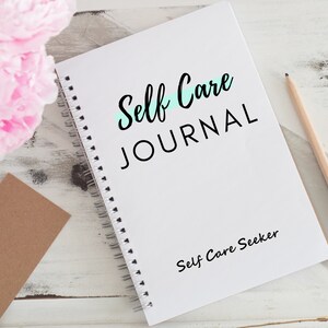 May include: A white spiral bound journal with the text "Self Care JOURNAL" in black lettering. A light blue line is drawn under the word "Self". The text "Self Care Seeker" is printed in black at the bottom of the journal.