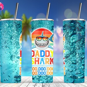 May include: A 20 ounce skinny tumbler with a blue and white design featuring a cartoon shark with sunglasses and the text "Daddy Shark" and "Doo Doo Doo Doo Doo Doo Doo Doo".
