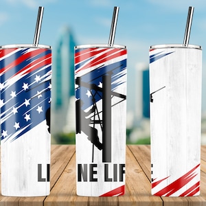 Könnte beinhalten: Ein Edelstahlbecher mit weißem Holzmaserungshintergrund und einem rot-weiß-blauen amerikanischen Flaggenmuster. Der Becher zeigt eine Silhouette eines Linienmannes, der an einem Strommast arbeitet, und den Text "LINE LIFE".