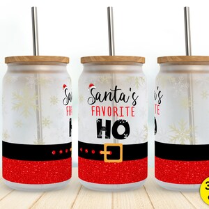 May include: Three 16 ounce glass tumblers with a Santa Claus theme. The tumblers are frosted and have a red glitter design. The middle tumbler has the text "Santa's Favorite HO" in black text.