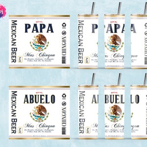May include: Two 20 ounce skinny tumblers with a white background and gold accents. The tumblers feature a Mexican beer label design with the text "Soy El Papa" and "Soy El Abuelo" and the words "Mexican Beer" and "Mas Chingon".