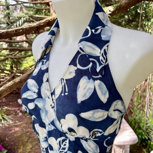 Peut inclure: Robe à col halter bleu marine avec un motif floral blanc et bleu clair. La robe est présentée sur un mannequin. Elle a un col en V et est sans manches, idéale pour l'été.