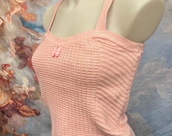 May include: A pink waffle knit tank top with thin straps and a small pink button detail on the front.