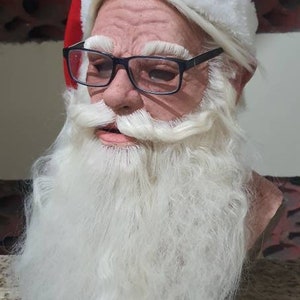 Puede incluir: Una máscara de Papá Noel con gorro rojo y blanco, gafas y barba blanca larga. La máscara tiene una apariencia realista, con arrugas y tonos de piel. Un artículo festivo para Navidad.
