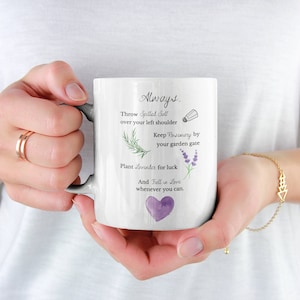 May include: White ceramic mug with a black handle. The mug features a handwritten message that reads "Always... Throw Spilled Salt over your left shoulder Keep Rosemary by your garden gate Plant Lavender for luck And Fall in Love whenever you can." The message is accompanied by illustrations of a salt shaker, rosemary, lavender, and a purple heart.