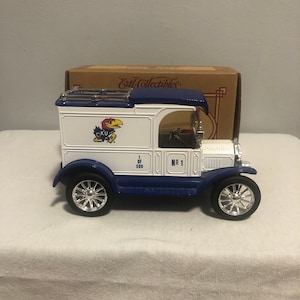 May include: A white and blue toy delivery truck with a blue roof and a University of Kentucky logo on the side. The truck has a chrome grill and wheels. The truck is numbered "1 of 500" and "No. 1".