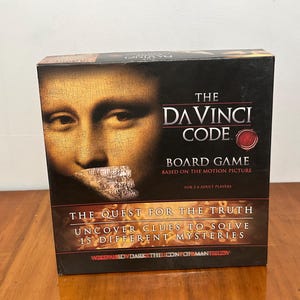 May include: The Da Vinci Code board game box. The box features the Mona Lisa painting and the game's title. The game is based on the motion picture and is for 2-6 adult players. The box reads: "The Quest for the Truth, Uncover Clues to Solve 15 Different Mysteries."