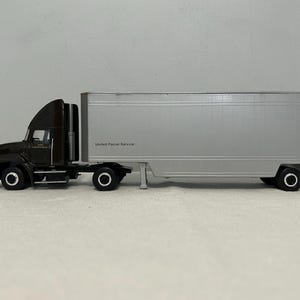 May include: A black and silver toy semi-truck with a trailer. The trailer has the words "United Parcel Service" printed on the side.