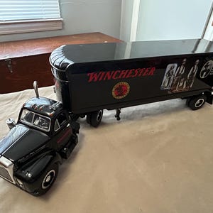 May include: Black toy semi-truck and trailer with the word "Winchester" on the side. The trailer has a graphic of people in period clothing.
