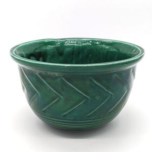 May include: A deep emerald green ceramic bowl featuring a glossy finish and a textured chevron pattern wrapping around the exterior. The bowl has a wide, rounded rim and a series of horizontal ridges encircling the base, creating a distinct profile.
