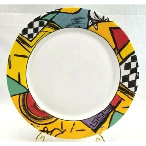 May include: A white ceramic dinner plate with a colorful geometric design. The rim of the plate features a yellow, red, green, blue, black, and white pattern.