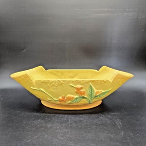 May include: A yellow ceramic planter with a floral design. The rectangular planter has a raised base and flared sides. Orange flowers and green leaves are embossed on the front. The planter is approximately 12 inches long.