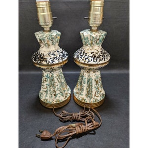 May include: A pair of vintage ceramic table lamps with a white, green, and black speckled glaze. The lamps have a gold trim and are wired with a brown cord and plug.