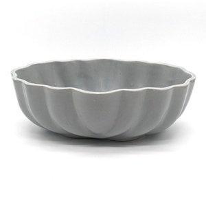 May include: A light gray, ceramic bowl with a scalloped rim. The bowl has a rounded, oval shape and a smooth, matte finish. The bowl is designed for serving food.
