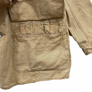 May include: A brown canvas jacket with a large flap pocket and multiple smaller pockets. The jacket has a worn, vintage look.