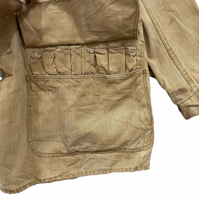 May include: A brown canvas jacket with a large flap pocket and multiple smaller pockets. The jacket has a worn, vintage look.