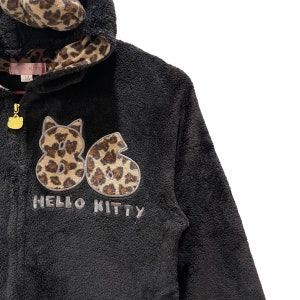 Peut inclure: Sweat-shirt &agrave; capuche en polaire noir avec une doublure de capuche en imprim&eacute; l&eacute;opard. Le devant pr&eacute;sente un grand motif brod&eacute; des chiffres "86" en imprim&eacute; l&eacute;opard avec le texte "HELLO KITTY" en dessous.