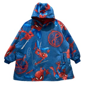 Puede incluir: Manta con capucha azul con un patr&oacute;n repetido del personaje de Spider-Man en rojo y azul. La manta tiene un forro interior rojo, una capucha y un bolsillo delantero. Los pu&ntilde;os son de color azul oscuro.