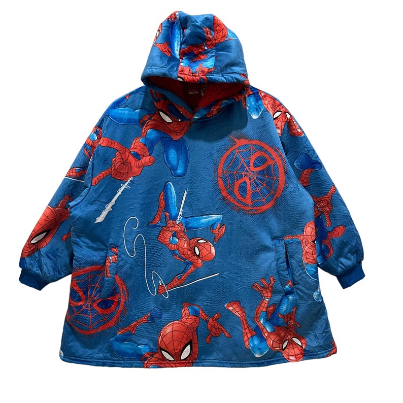 Puede incluir: Manta con capucha azul con un patr&oacute;n repetido del personaje de Spider-Man en rojo y azul. La manta tiene un forro interior rojo, una capucha y un bolsillo delantero. Los pu&ntilde;os son de color azul oscuro.