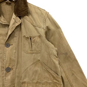 May include: A tan work jacket with a corduroy collar and multiple pockets. The jacket has a button-up front and is made of a durable fabric.