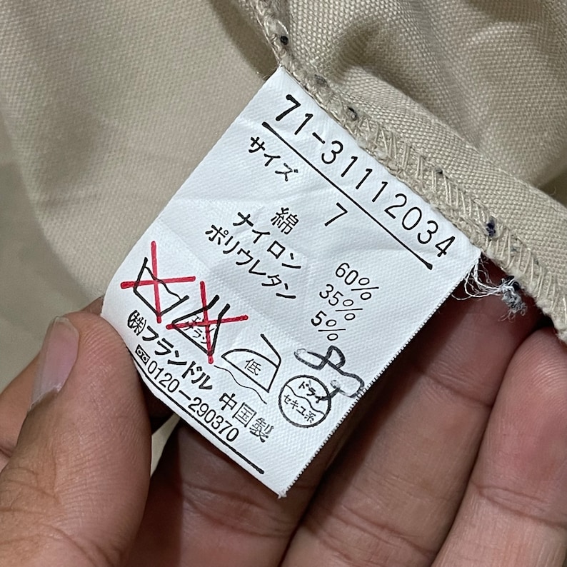 May include: Close-up of a clothing tag with Japanese text and numbers. The tag displays fabric composition percentages: 60% cotton, 35% nylon, and 5% polyurethane. Washing instructions are also visible.