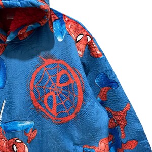 Puede incluir: Manta con capucha azul con gr&aacute;ficos de Spider-Man. La manta presenta un dise&ntilde;o de telara&ntilde;a roja y m&uacute;ltiples im&aacute;genes de Spider-Man. La capucha est&aacute; forrada con tela roja. La manta est&aacute; hecha de un material suave y texturizado.