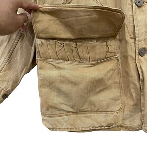 May include: A brown utility jacket with a large flap pocket on the front. The pocket has a pleated detail and a smaller pocket on the front.