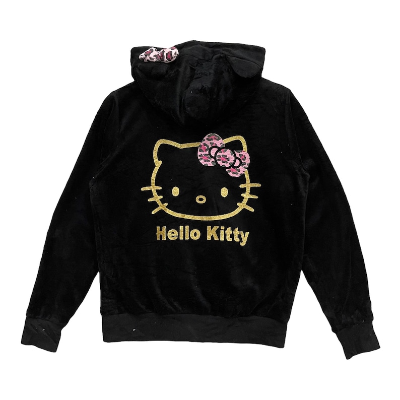Pode incluir: Camisola de veludo preto com capuz, com um gr&aacute;fico Hello Kitty dourado e um la&ccedil;o rosa. O capuz tem orelhas de estampa de leopardo.