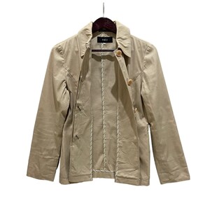May include: Tan jacket with a collared neckline and button closures. The jacket has long sleeves and a tailored fit. The brand name "INED" is visible on the label. The jacket is hanging on a wooden hanger against a white background.