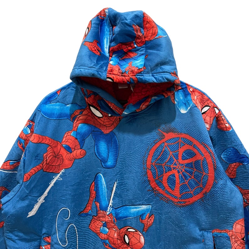Puede incluir: Sudadera con capucha azul con un patr&oacute;n repetido del personaje de Spider-Man en rojo y azul. El dise&ntilde;o incluye a Spider-Man en varias poses de acci&oacute;n y un gr&aacute;fico de telara&ntilde;a roja. El forro interior es rojo.