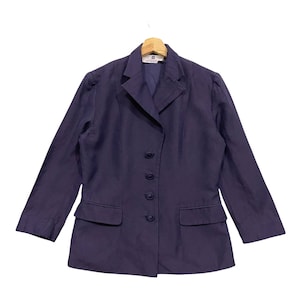 Pode incluir: Um blazer azul marinho com lapela entalhada, fecho de quatro botões e dois bolsos frontais. O blazer está pendurado em um cabide de madeira. O nome da marca é visível na parte superior das costas do blazer.