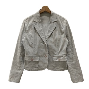 Puede incluir: Un blazer gris claro con cierre de un solo bot&oacute;n, dos bolsillos delanteros y mangas largas. El blazer est&aacute; hecho de una tela texturizada y se muestra en una percha de madera sobre un fondo blanco. El blazer tiene un dise&ntilde;o cl&aacute;sico y entallado.