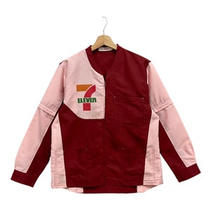 Puede incluir: Chaqueta bicolor en granate y rosa claro, con el logo de 7-Eleven en el pecho izquierdo. La chaqueta tiene cuello en V y dos bolsillos delanteros. Las mangas y la parte superior son rosa claro, el resto es granate.