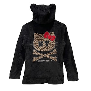 Peut inclure: Sweat-shirt &agrave; capuche noir avec un motif Hello Kitty imprim&eacute; l&eacute;opard avec un cr&acirc;ne et des os crois&eacute;s. Le texte "Hello Kitty" est imprim&eacute; sous le motif.