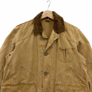 May include: A brown work jacket with a corduroy collar and multiple pockets. The jacket has a button closure and is made of a durable fabric.