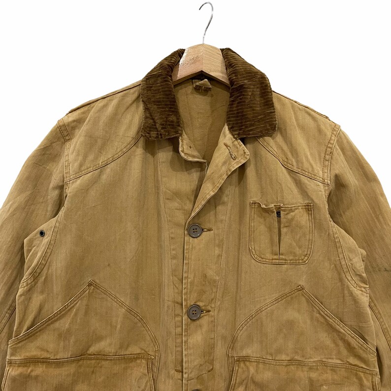 May include: A brown work jacket with a corduroy collar and multiple pockets. The jacket has a button closure and is made of a durable fabric.