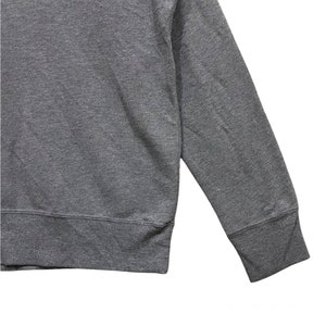 May include: A close-up of a gray sweatshirt. The sweatshirt has a crew neck and long sleeves with ribbed cuffs. The fabric appears to be a soft, medium-weight material.