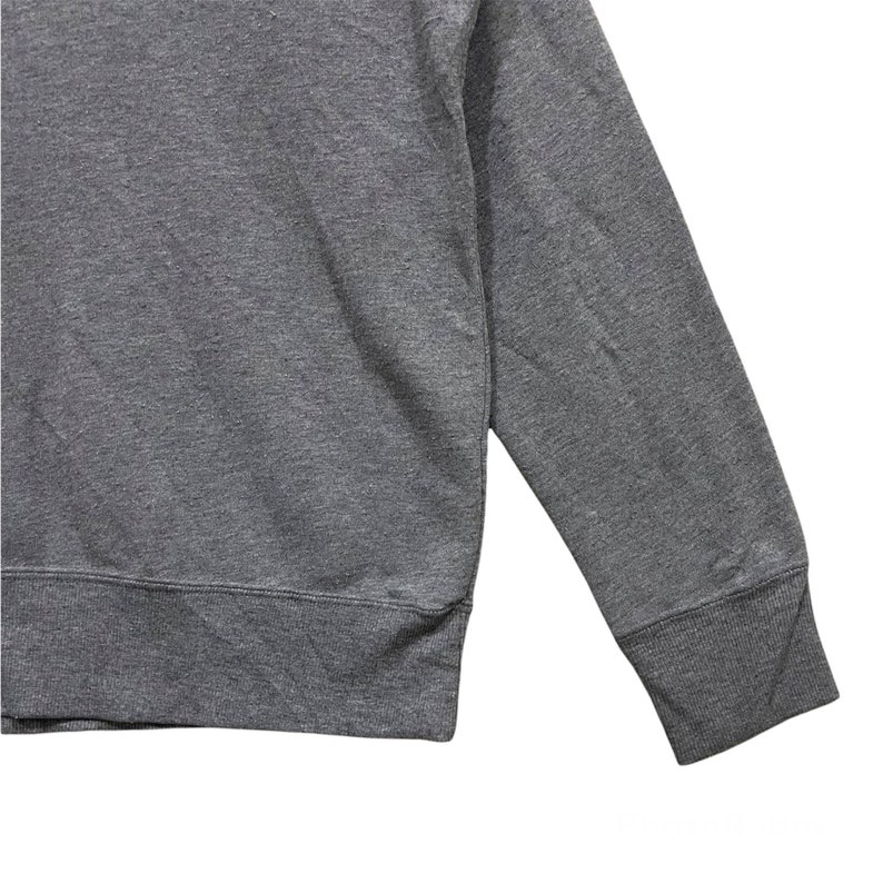 May include: A close-up of a gray sweatshirt. The sweatshirt has a crew neck and long sleeves with ribbed cuffs. The fabric appears to be a soft, medium-weight material.