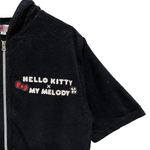 May include: Black zip-up hooded sweatshirt with the text "HELLO KITTY x MY MELODY" in white, a red bow and flower graphic. The short-sleeved sweatshirt has a full-length zip.