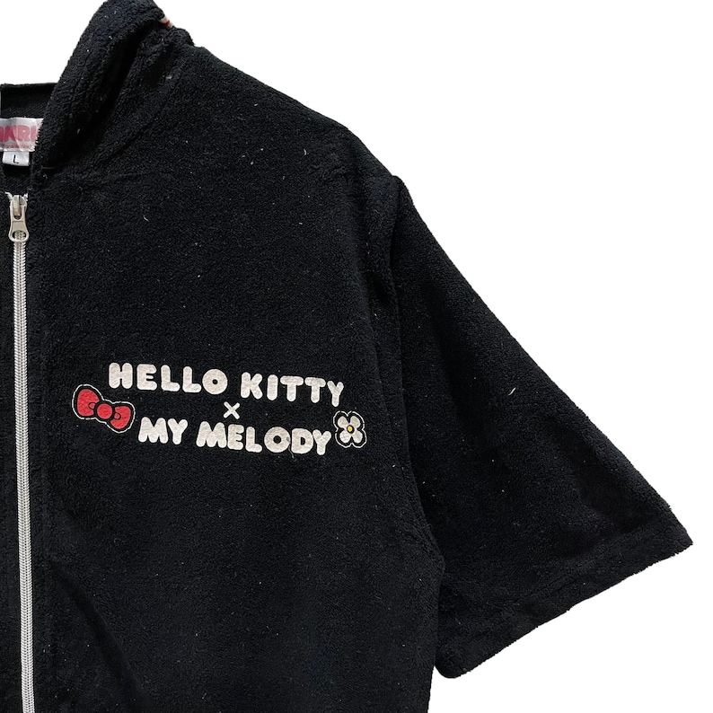May include: Black zip-up hooded sweatshirt with the text "HELLO KITTY x MY MELODY" in white, a red bow and flower graphic. The short-sleeved sweatshirt has a full-length zip.
