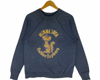 May include: A dark gray sweatshirt with a vintage-style graphic of a cartoon gopher wearing a hat. The graphic says "Minnesota Golden Gophers".