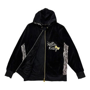 May include: Black velour zip-up hoodie with a Hello Kitty design featuring a yellow bow. The hoodie has a zebra print on the sleeves and a black lining.