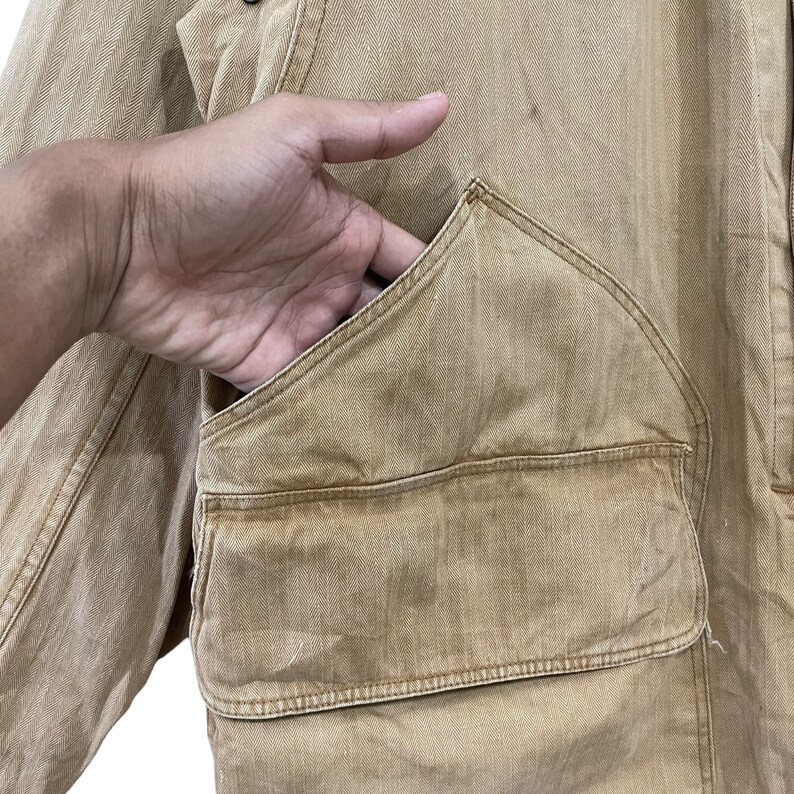 May include: A tan utility jacket with a large, angled pocket on the front. The pocket has a flap and a button closure.