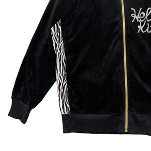 May include: Black velour jacket with a zipper closure and a zebra print panel on the side. The jacket has a gold zipper and the text "Hello Kitty" is embroidered on the right side.