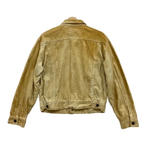 May include: Rear view of a tan corduroy jacket with a button-down closure. The jacket features a classic collar, long sleeves, and two buttoned pockets. The corduroy fabric has vertical ridges.
