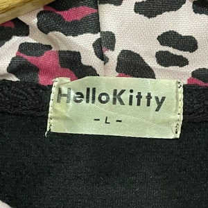 Pode incluir: Casaco de moletom preto com capuz de estampa de leopardo rosa e preto e uma etiqueta branca que diz "Hello Kitty - L - "