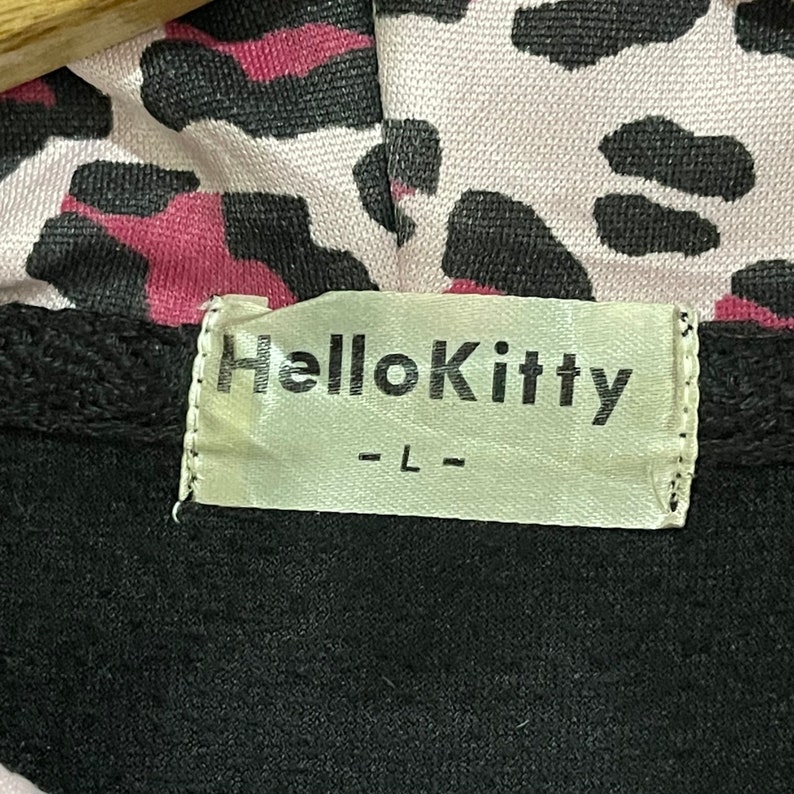 Pode incluir: Casaco de moletom preto com capuz de estampa de leopardo rosa e preto e uma etiqueta branca que diz "Hello Kitty - L - "